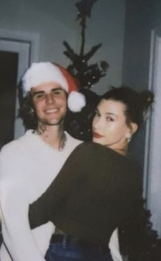 a man and woman are standing in front of a christmas tree with a santa hat on