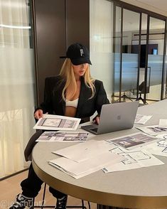 a woman sitting at a table with a laptop in front of her and papers around her