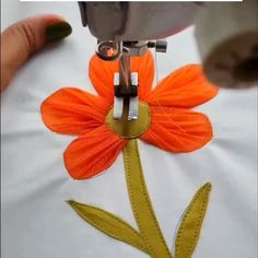 an orange flower being sewn on to a white t - shirt with yellow stitching