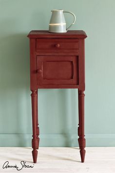 a small red table with a white vase on top and a blue wall behind it