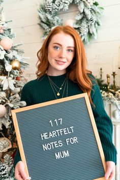 a woman holding a sign that says 17 heartbeat notes for mum in front of a christmas tree