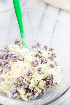 a glass bowl filled with blueberries and cream cheese dressing next to a green plastic spoon