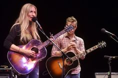 a man and woman playing guitars on stage