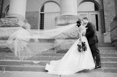 a bride and groom kissing in front of a building on their wedding day with veil blowing in the wind