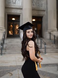 a woman in a graduation cap and gown poses for a photo outside an old building