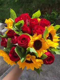 a bouquet of sunflowers and red roses in a woman's hand on the ground