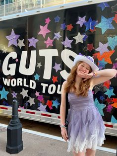 a woman in a purple dress and hat standing next to a bus with stars on it