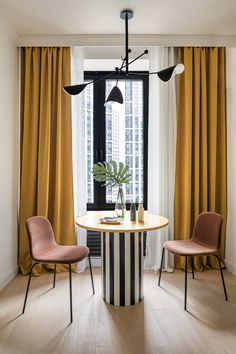 two chairs and a table in front of a window with yellow drapes on the windowsill