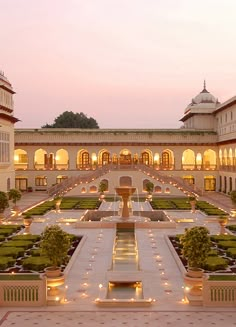 an outdoor courtyard at dusk with lights on the ground and plants in the center surrounded by hedges