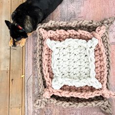 a dog laying on the floor next to a crocheted rug with a pillow