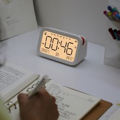 a person writing on a notepad in front of an alarm clock with the time displayed