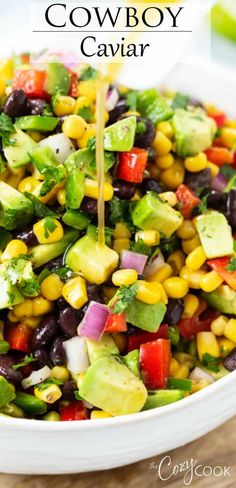 a white bowl filled with corn, avocado and black bean salad on top of a wooden table