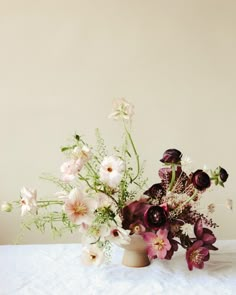 a vase filled with lots of flowers sitting on top of a white tablecloth covered table