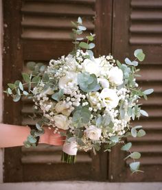 a bridal bouquet with white flowers and greenery in front of a wooden door