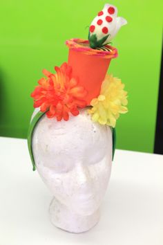 a white mannequin head with an orange hat and flowers on it