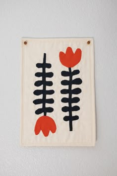 an embroidered wall hanging with black and red flowers on it's side, against a white wall