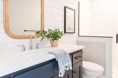 a white toilet sitting next to a bathroom sink under a mirror and a wooden framed mirror