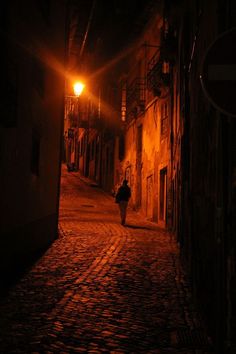 a person walking down an alley way at night with a street lamp on the side