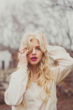 a woman with long blonde hair wearing a white shirt and holding her hands to her head