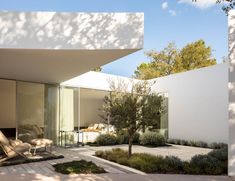 an outdoor patio with lounge chairs and trees in the back ground, next to a white building