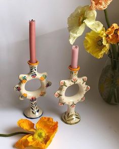 two vases with candles and flowers in them on a white surface next to each other