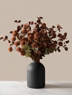 a vase filled with lots of brown flowers on top of a white countertop next to a wall