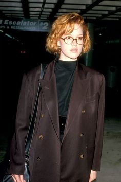 a woman wearing glasses and a black jacket is standing in an airport with her hand on her hip