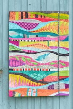 a colorful quilt hanging on the side of a wooden wall next to a blue door