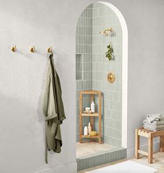 a bathroom with a green tiled shower and wooden shelf next to the bathtub is shown