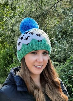 a woman wearing a green and white knitted hat with blue pom - pom