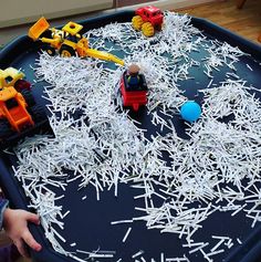 a child is playing with shredded paper in a play table filled with toy trucks and construction vehicles