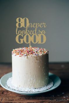 a white cake with gold lettering and sprinkles is on a wooden table