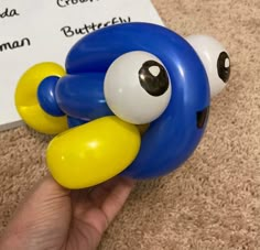 a hand holding a blue and yellow balloon with googly eyes