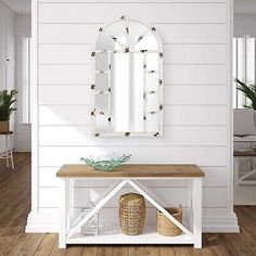 a white table with a mirror on it and some plants in front of the wall