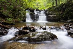 a small waterfall in the middle of a forest filled with rocks and water flowing down it's sides