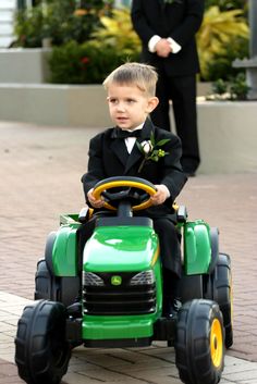 a young boy in a tuxedo riding on a toy tractor