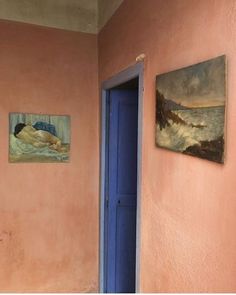 two paintings hang on the wall next to a blue door in a pink walled room