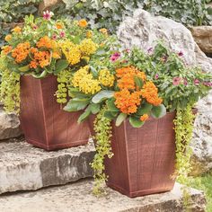 two metal planters with flowers in them sitting on some stone steps next to rocks