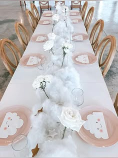 a long table is set with pink plates and white napkins, flowers on them