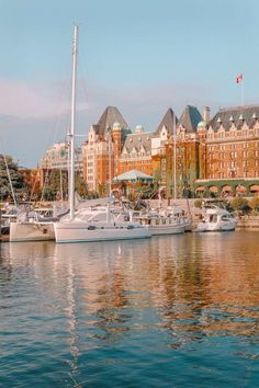 several sailboats are docked in the water near some large buildings and a flag pole