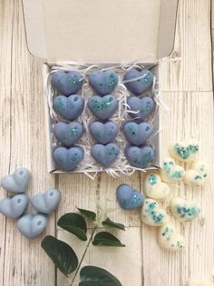 blue and white heart shaped cookies in a box next to some green leafy plants