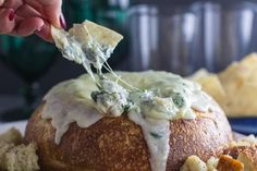 a person dipping some kind of food into a bread bowl with cheese and sauce on it