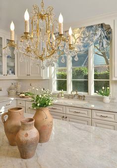 two vases sitting on top of a marble counter in a kitchen with chandelier