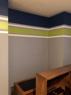 an empty room with blue, green and white stripes on the wall behind a wooden shelf