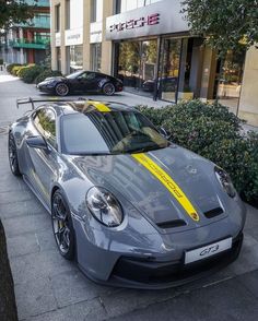 a grey sports car parked in front of a building with yellow stripes on the side