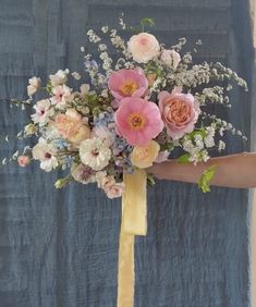 a woman holding a bouquet of flowers on her arm with a yellow ribbon tied around it