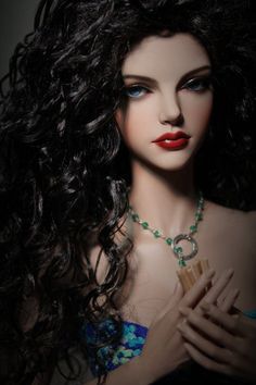 a mannequin with long black hair wearing a necklace and holding a wooden stick