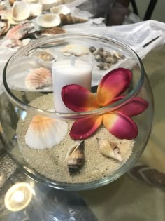 a glass bowl filled with sand and flowers on top of a table next to candles