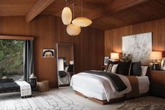 a bedroom with wood paneling, white bedding and two lamps hanging from the ceiling