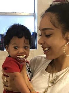 a woman holding a child in her arms and smiling at the camera while wearing gold teeth